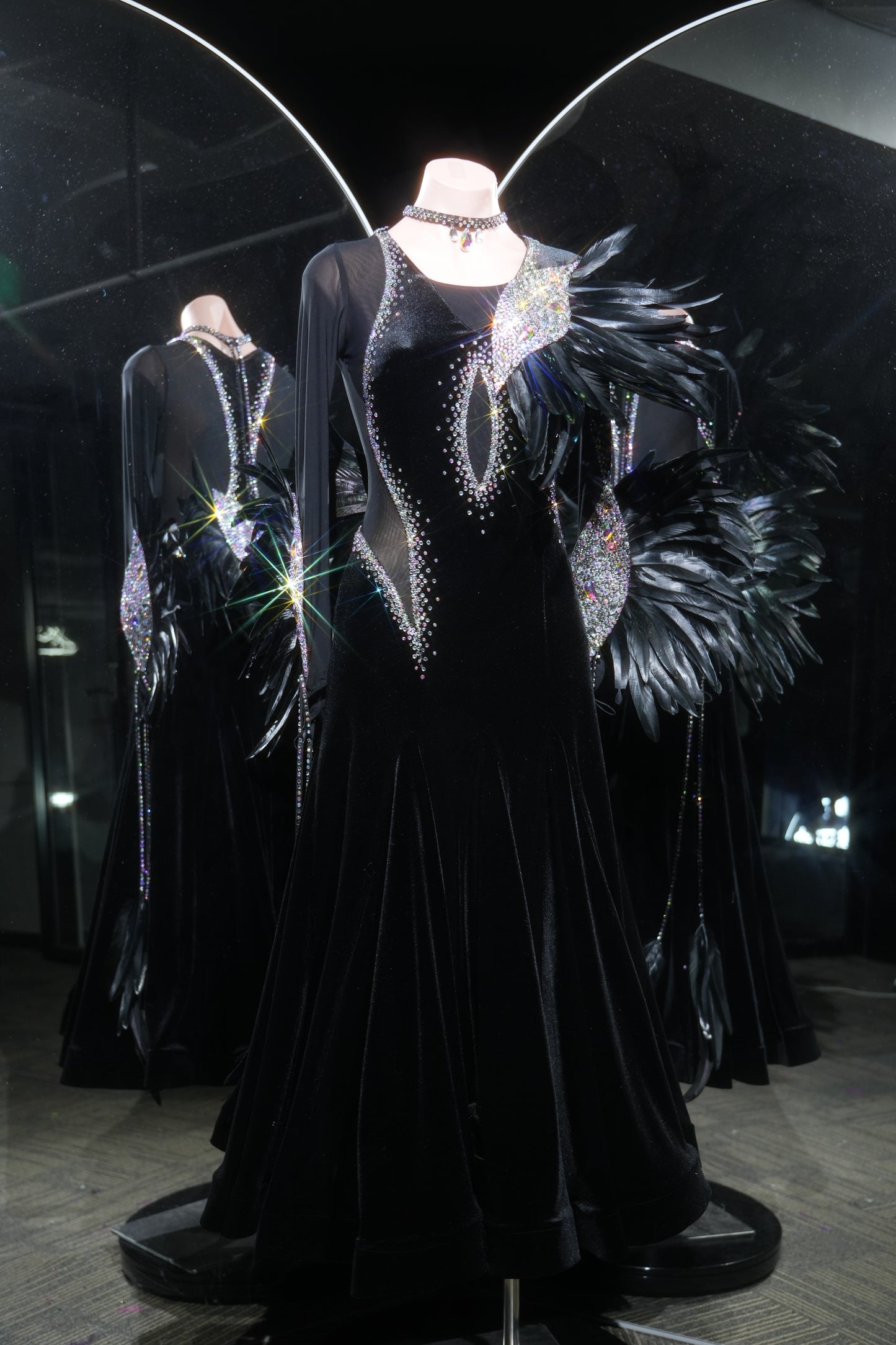 Black evening gown with intricate detailing on a mannequin in a darkly lit room.