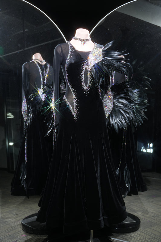 Black evening gown with intricate detailing on a mannequin in a darkly lit room.