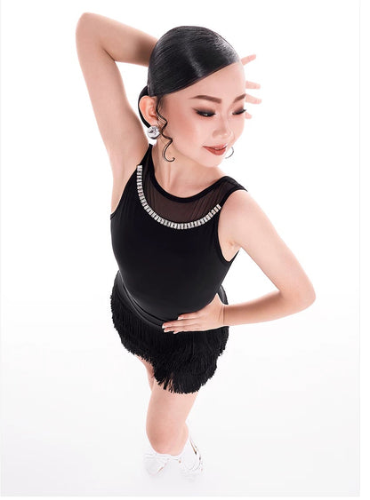 A woman modeling a black sleeveless ballroom dance leotard with a sheer mesh neckline and a black fringe skirt, posed against a white studio background with the brand name 'DUNYO DESIGN' printed above.
