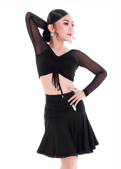 A woman modeling a black dancewear set consisting of a long-sleeve crop top with sheer sleeves and a matching flared skirt, shown against a white background with the brand name 'DUNYO DESIGN' at the top.