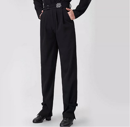 A model wearing black BOBO DANCE high-waisted dance pants with a matching black belt featuring a silver 'BD' logo, paired with a black long-sleeve top and black dance shoes, against a light gray background.