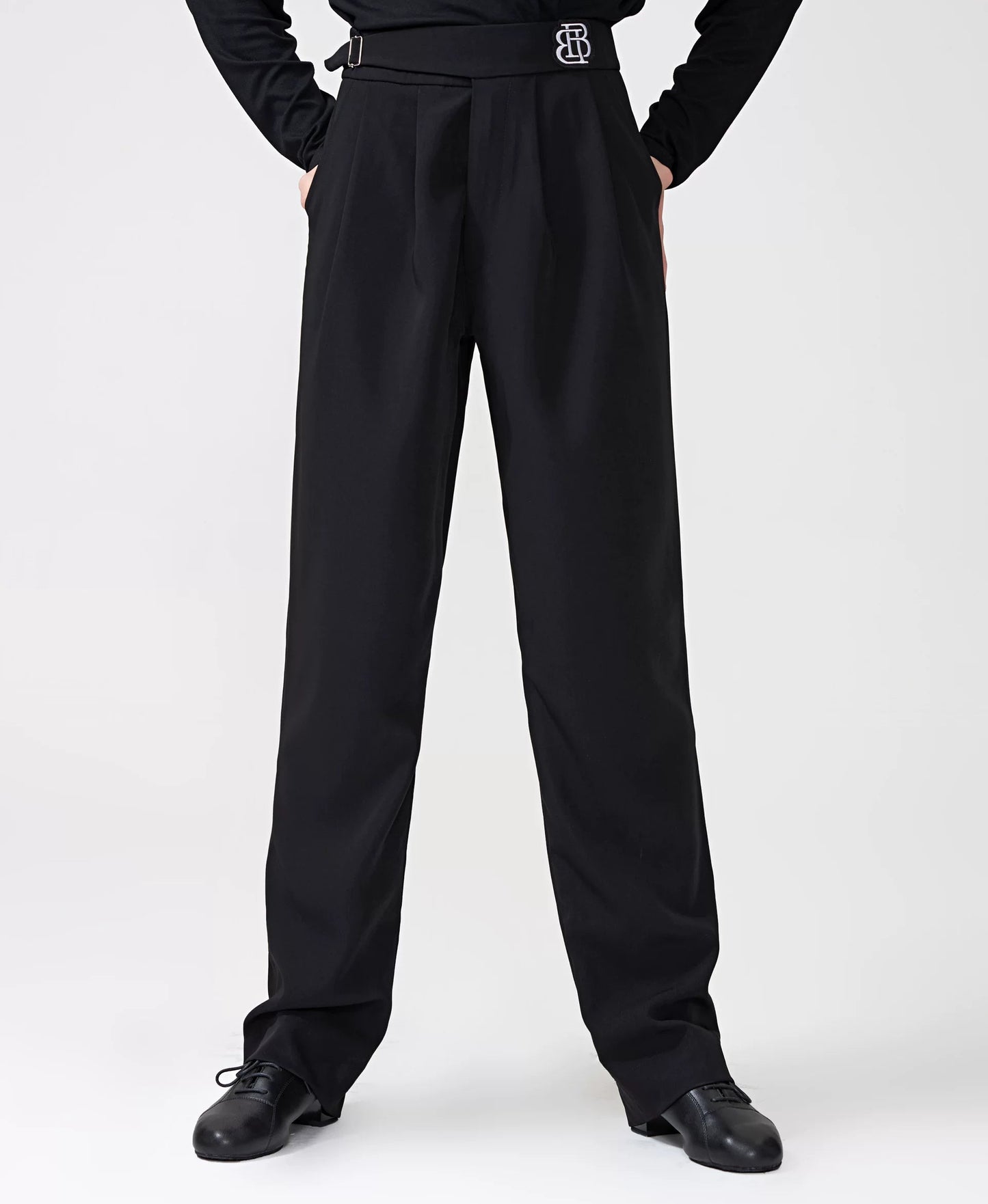 A model wearing a black long-sleeve top and matching high-waisted black trousers with a decorative silver 'BB' logo belt buckle, standing against a light gray studio background. The BOBO DANCE brand logo is visible in the top left corner.