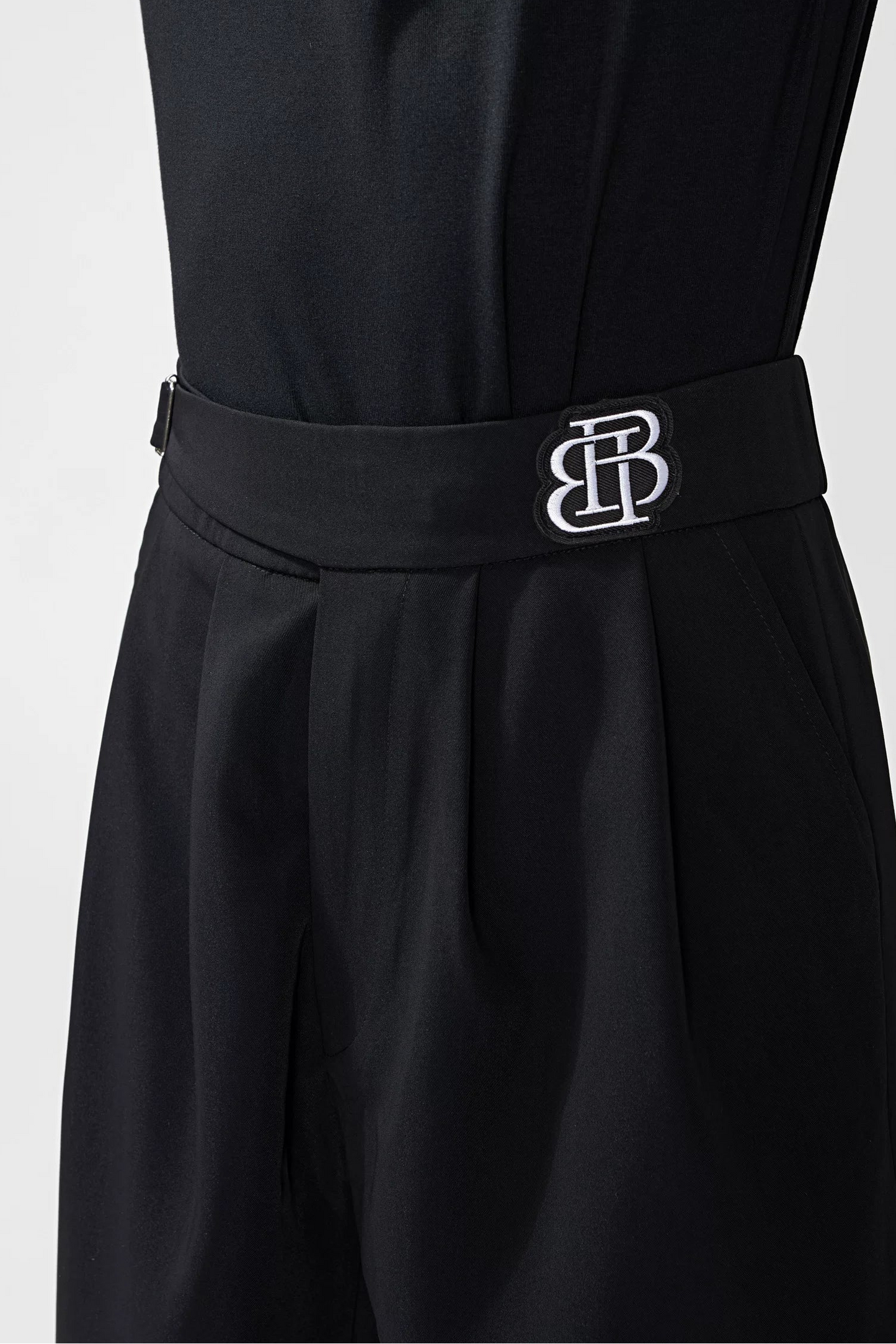 A close-up of a black BOBO DANCE jumpsuit featuring a matching black waist belt with a silver interlocking 'BD' logo, shown on a model against a light gray background.